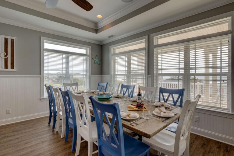 Wooden dining table with chairs in a bright dining room with large windows at Living the Dream